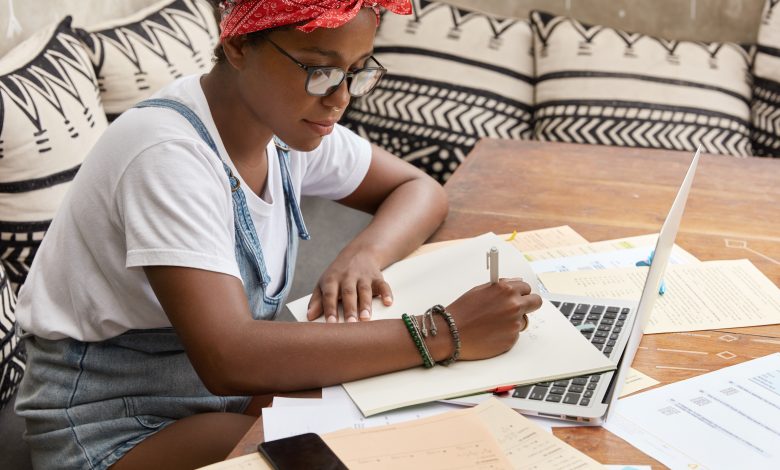 sideways shot of black busy female journalist studies papers for writing article